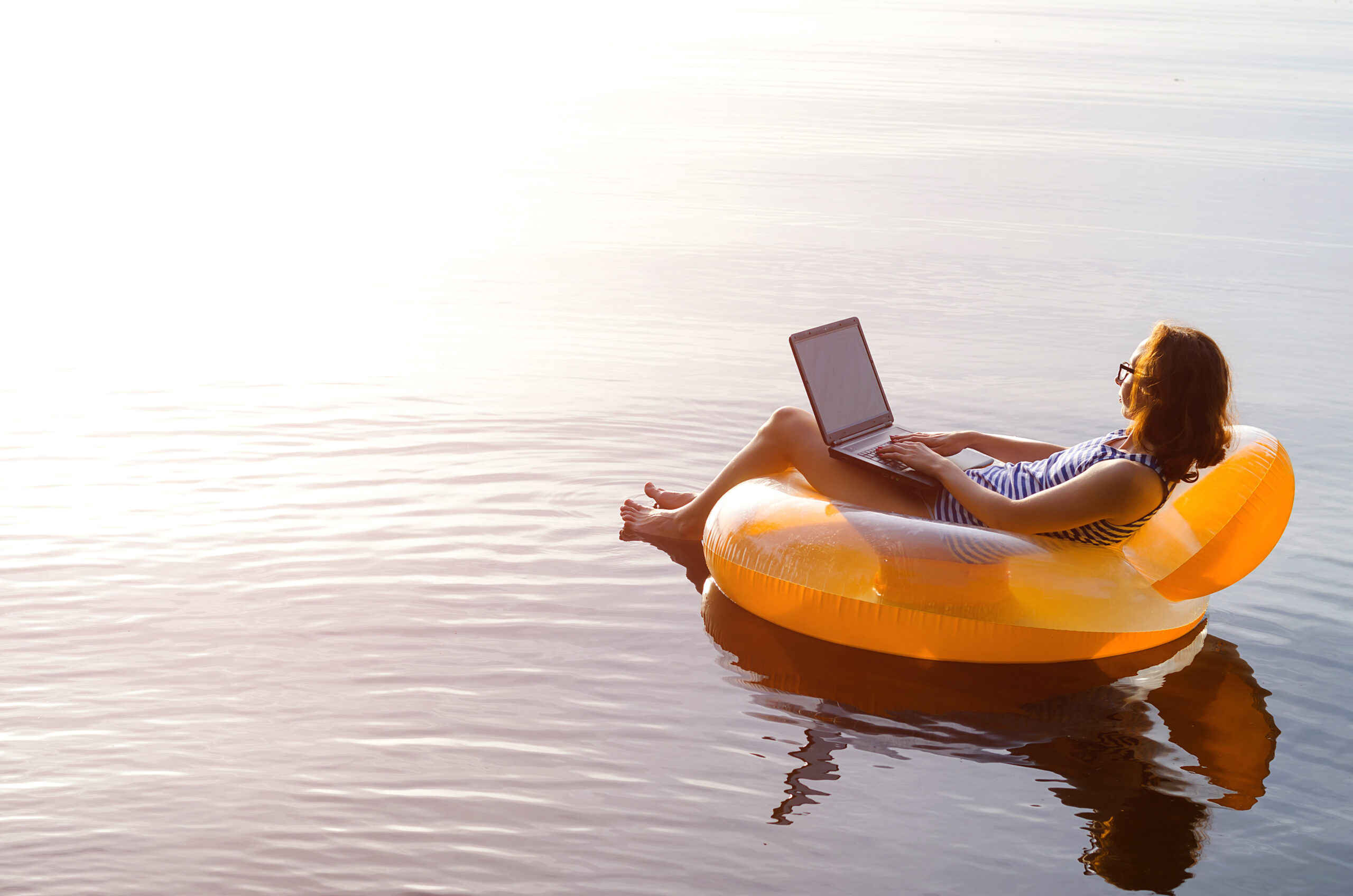 Business woman working on a laptop in an inflatable ring in the water, a copy of the free space. Workaholic, work on vacation.